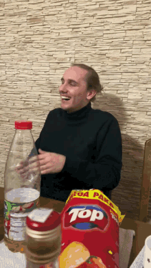 a man sits at a table with a bag of top chips in front of him