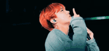 a man with red hair is pointing up with his finger while wearing headphones .