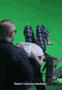 a man is sitting next to a woman who is laying on a green screen .