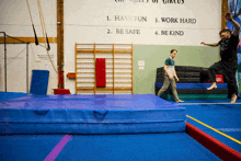 a man is jumping on a balance beam in front of a wall that says have fun work hard be safe and be kind