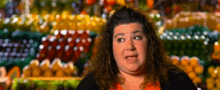 a woman making a funny face in front of a fruit stand .
