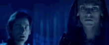 a man in a hooded jacket is standing next to a woman in a dark room