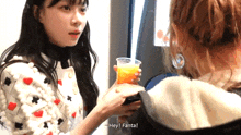 a woman is holding a cup of orange juice while another woman says hey fanta