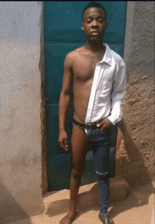 a shirtless man in shorts and a white shirt stands in front of a blue door