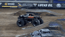 a monster truck is driving down a dirt track in front of a lucas oil sign