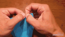 a close up of a person 's hands holding a piece of blue paper that says made in animatica on the bottom