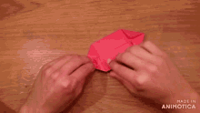 a person is making a red origami object with the words made in animotica below them