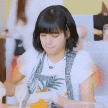 a young woman wearing a white shirt and overalls is sitting at a table