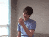 a young man in a blue shirt is holding a piece of paper in his hand and making a funny face .