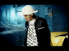a man wearing a hat and a jacket is standing next to a yellow car .