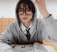 a young man wearing glasses and a hoodie is sitting at a table