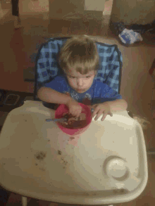 a little boy in a high chair is eating from a pink bowl