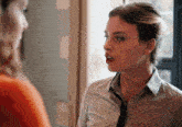 a woman wearing a tie and a white shirt talks to another woman