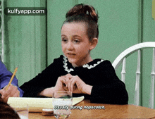 a young girl is sitting at a table with a glass of water and a notebook .