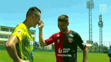 two soccer players shaking hands with one wearing a plus art jersey