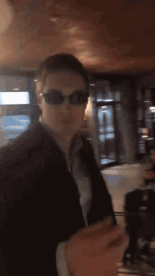 a man wearing sunglasses and a suit is standing in a room