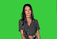 a woman in a black and white striped shirt is giving a thumbs up on a green screen .