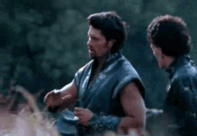 two men are standing next to each other in a field and talking .