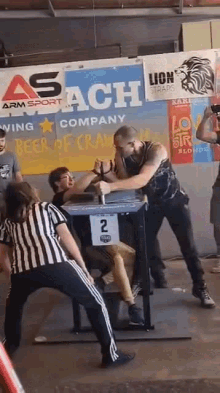 a man is arm wrestling with a referee in front of a sign that says asach