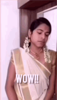a woman in a sari is standing in front of a window and says wow .