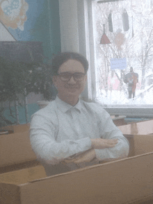 a man in a white shirt and glasses sits in front of a window with a sign that says ' russian ' on it