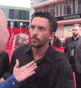 a man is talking to another man in front of a building that says shopper
