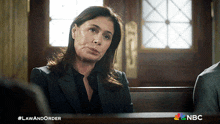 a woman in a suit sits in a courtroom next to a sign that says law and order