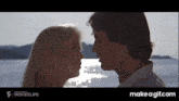 a man and a woman are kissing in front of a body of water and the words make a gif.com are on the bottom
