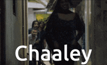 a woman in a black dress is walking through a doorway with the word chaaley on it