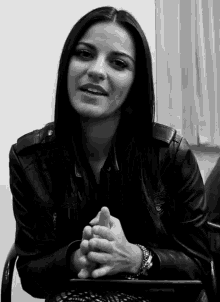 a woman in a leather jacket is sitting with her hands folded