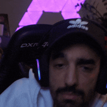 a man wearing headphones and an adidas hat looks at the camera