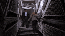 a man and a woman are walking up a set of stairs holding hands .