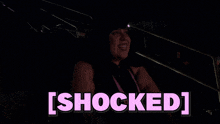 a woman is sitting in a dark room with the words [ shocked ] written above her