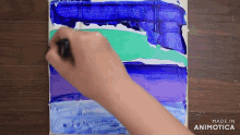 a person is painting a blue and green painting on a wooden table .