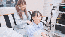 two girls are sitting on a couch and one has her hands on the other 's back