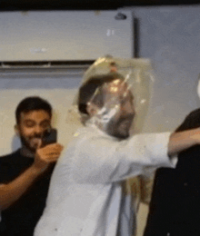 a man wearing a plastic bag on his head is being photographed by another man