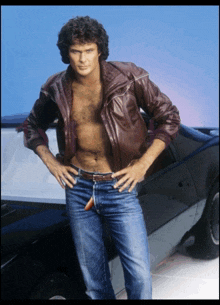 a man without a shirt is standing in front of a car with his hands on his hips
