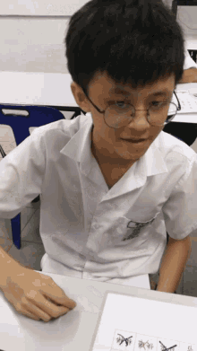 a young boy wearing glasses sits at a desk with a piece of paper that says ' x ' on it