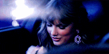 a woman wearing earrings is sitting in the back seat of a car at night .