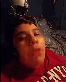 a young boy wearing a red shirt that says ny is laying on a bed with a football helmet in the background .