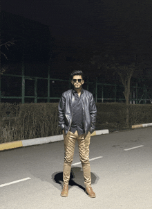 a man wearing sunglasses and a leather jacket stands on the side of the road