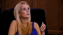 a woman in a blue top is sitting in a chair and holding a small object in her hand .