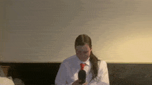 a woman in a white shirt and red tie is holding a black object