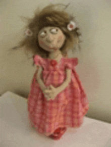 a doll in a pink dress with flowers in her hair is standing on a table .