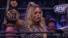 a woman in a checkered shirt is holding a wrestling championship belt in a ring .