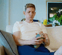 a man is sitting on a couch holding a cup and making a face