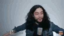 a man with long hair and a beard is holding a cell phone and talking into a microphone .