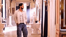 a man in a white shirt and blue jeans is standing in a hallway next to a statue .