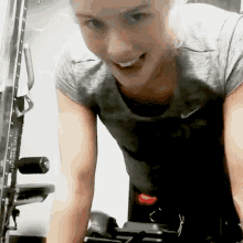 a woman in a grey nike shirt is smiling while riding a bike