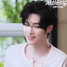a young man wearing a white shirt and a silver necklace is smiling .